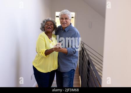 Portrait of cheerful multiracial senior friends dancing by wall in corridor at nursing home Stock Photo