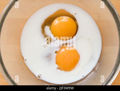 Milk added to two raw chicken eggs yolks in a glass bowl, ready to make scrambled egg. Egg and milk mixture Stock Photo