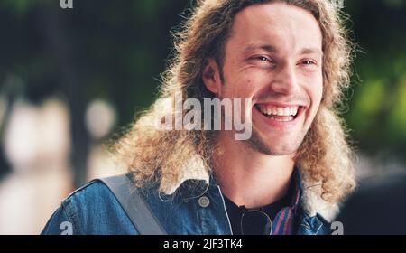 A cheerful handsome man with curly hair in the park. A happy young man laughing relaxing outside in the park. A young handsome man with blonde curly Stock Photo