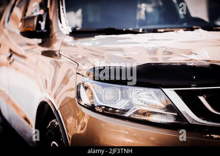 The front part of a new polished beautiful silver-colored car with snow on the bumper on a sunny day. Transport in winter. Stock Photo