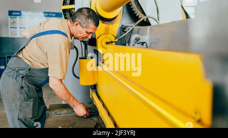 Worker cuts metal sheets on mechanical guillotine machine in production hall. Industrial equipment for metal cutting. Real scene. Real workflow. Man at work. Stock Photo