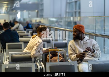 International couple sitting in airport lounge smiling, look at each other, talk, waiting departure. Stock Photo