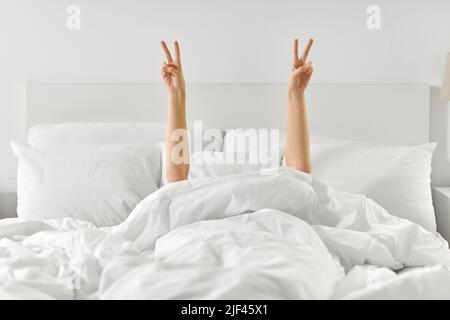 hands of woman lying in bed and showing peace Stock Photo
