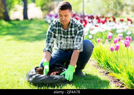 man with soil in bag and flowers working at garden Stock Photo