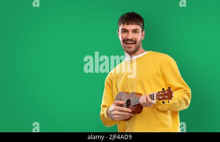 happy man playing ukulele guitar over green Stock Photo