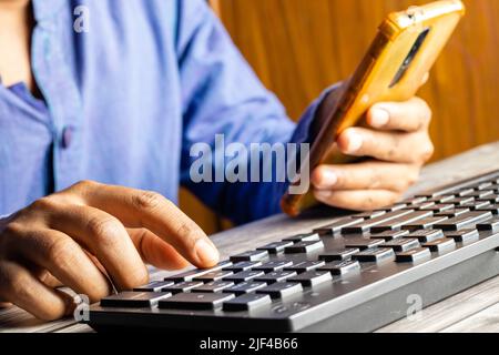 Selective focus on an Indian male hand using mobile phone to enter one time password in front of computer Stock Photo