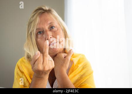 Middle aged Caucasian woman by a window. Woman in her house with casual dress. Stock Photo