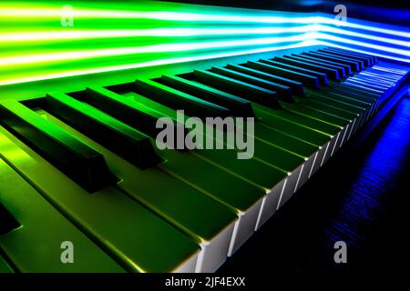 A closeup of the piano keyboard illuminated by green and blue neon lights. Stock Photo