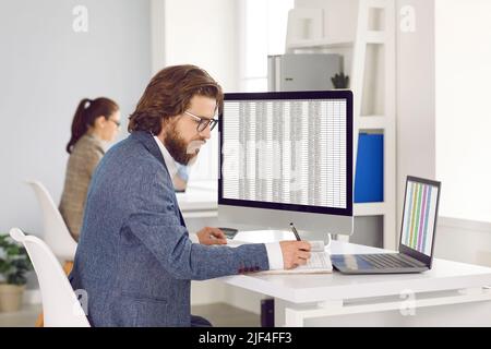 Caucasian man works as accountant or auditor sits at table with computers in open space office Stock Photo