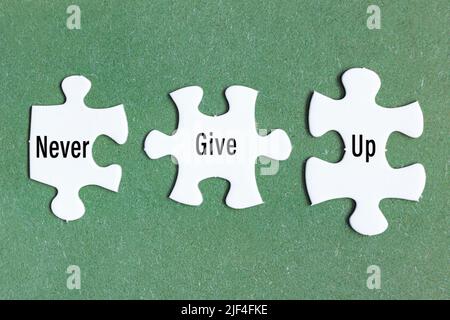 Motivational text on three pieces of white jigsaw puzzle on green background. Stock Photo