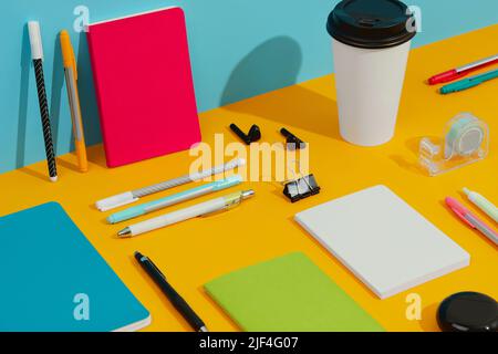 Colorful notepads, pens and paper cup on orange table Stock Photo