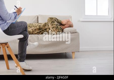 Soldier who suffers from PTSD lying on sofa and talking to therapist or psychologist Stock Photo