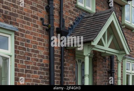 Green apex porch over the front door with red brick walls and black painted drain pipes Stock Photo