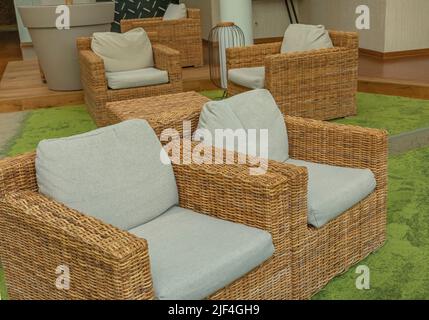 Rattan arm chairs with grey cushions and green carpet making a nice peaceful relaxation area indoors Stock Photo