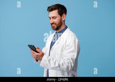 Smiling medical specialist using mobile phone over blue studio background Stock Photo