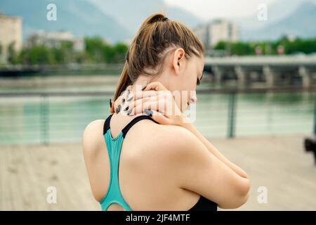 Young beautiful woman wearing sportive clothes on city park, outdoors feeling hurt joint shoulder back pain ache, fibromyalgia concept, close up rear Stock Photo