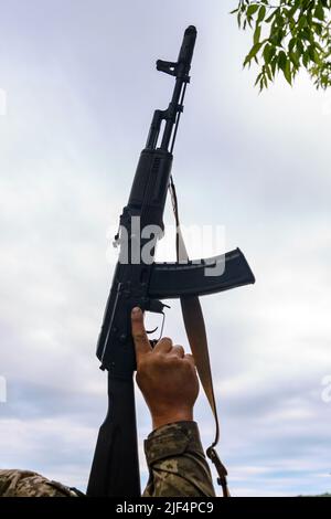 The Ukrainian military holds a submachine gun. hand with a machine gun on a background of sky. Stock Photo