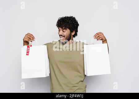 Young middle eastern man laughing while posing with shopping bags isolated over white wall Stock Photo