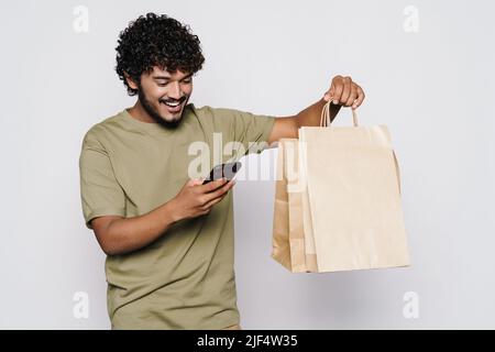 Young middle eastern man with shopping bags using cellphone isolated over white wall Stock Photo