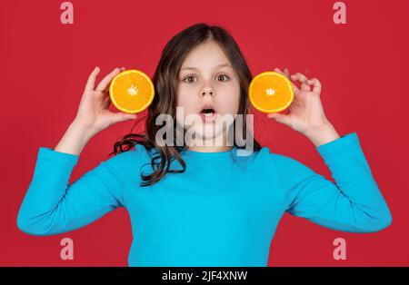 shocked teen kid holding orange fruit on purple background Stock Photo