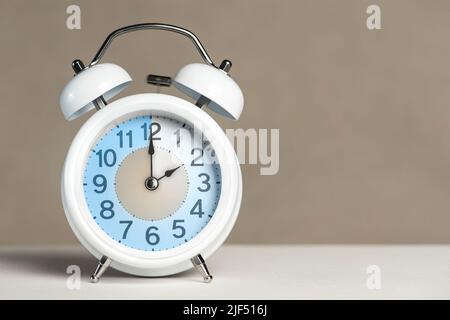 Two hours on the alarm. A white alarm clock is on a white table. The clock hand points to 2 o clock. Change time. Set an alarm for 2 00 or 14 00. copy Stock