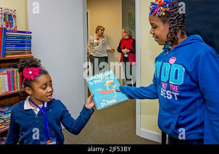 An African-American girl gives a Dr. Seuss book to a younger child during an after-school program, Feb. 28, 2013, in Columbus, Mississippi. Stock Photo