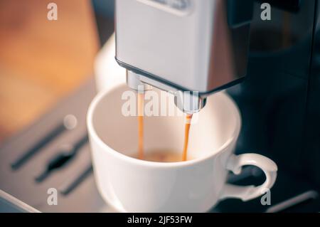 Modern coffee machine with a partially full cup of coffee on table in kitchen Stock Photo