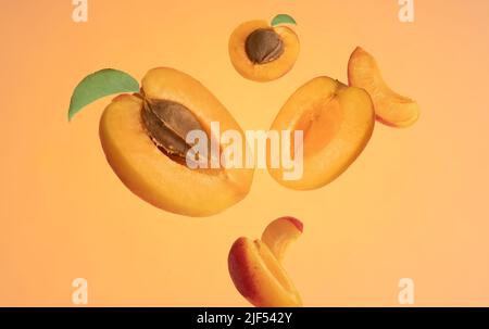 Close up studio macro photo of half and sliced ripe floating apricots on orange yellow background. Stock Photo
