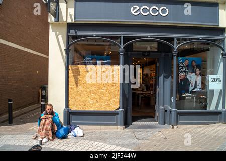 Homeless man begs outside a shop as public passes by Stock Photo Alamy