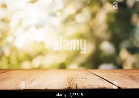 Empty wooden plank or deck, table top with background of blurred green trees, garden with sunlight or blurred foliage backyard. Nature with bokeh light. Mock up, template for product display, montage Stock Photo
