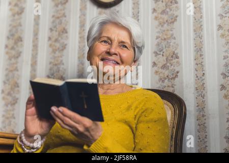 cute Caucasian grandmother holding the Bible and smiling satisfied medium closeup indoor spirituality concept. High quality photo Stock Photo