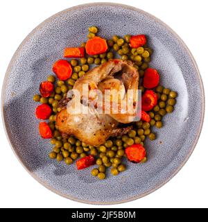 Oven baked quail served on plate with carrot slices and green peas Stock Photo