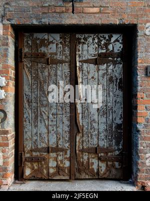 Old weathered metal double doors with heavy rust and peeling paint set in a red brick industrial wall Stock Photo