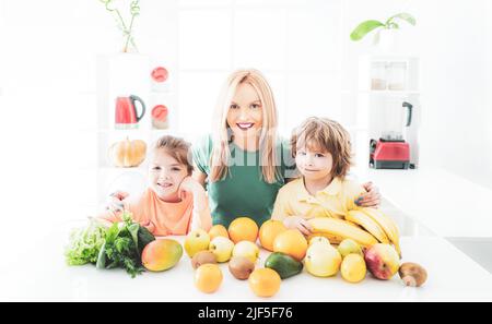 Happy laughing children and her beautiful young mother making fresh strawberry and other fruit juice in kitchen. Happy loving family. Stock Photo