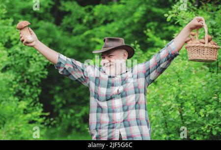 Picking mushrooms. Happy Grandfather - summer and hobbies. Old man walking. Grandpa Pensioner. Senior hiking in forest. Stock Photo