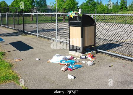 Trash bin overflowing with garbage beside a sport court in a local park. Stock Photo
