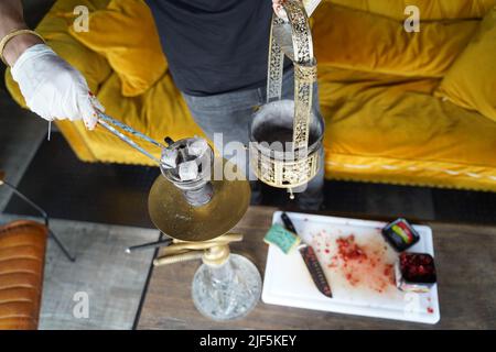 Berlin, Germany. 29th June, 2022. Glowing coal is placed on a shisha. As of July 1, only 25-gram packages of hookah tobacco will be allowed on the German market. According to information from an industry association, however, the approximately 100 German manufacturers of the tobacco have not had enough time to convert their production - which is why far too little hookah tobacco could come onto the market in the coming months. Credit: Joerg Carstensen/dpa/Alamy Live News Stock Photo