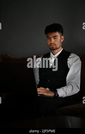 Professional male financial investment consultant manager or businessman in formal suit sits on leather sofa and uses a laptop computer. Stock Photo