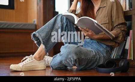 A young female college student sitting in the library floor and reading a book. cropped image. Education concept Stock Photo