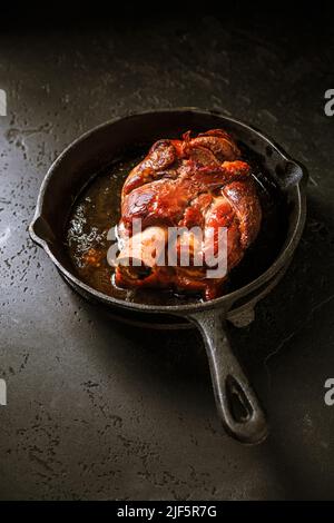 Traditional German cuisine - Roasted pork knuckle eisbein (Schweinshaxe) in iron pan on black background Stock Photo