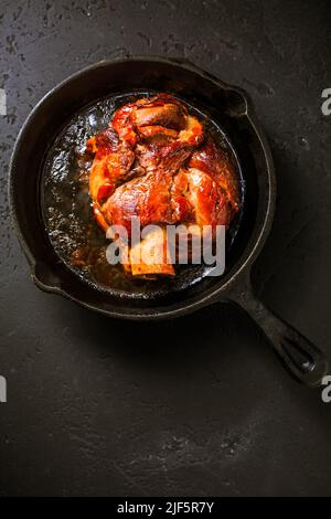 Traditional German cuisine - Roasted pork knuckle eisbein (Schweinshaxe) in iron pan on black background Stock Photo