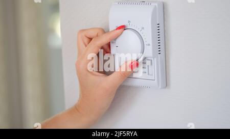 Woman's hand regulating the temperature of central heating of house on thermostat Stock Photo