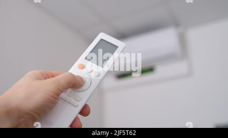 Hand with remote control is directed to air conditioner on wall Stock Photo