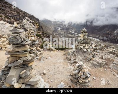 Rocks cairns (4500m) mark a viewpoint along the ridge to Nangkartshang Peak (5073m) above Dingboche with low May clouds over the Imja Khola, Khumbu. Stock Photo