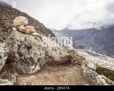 Rock cairn on a boulder T 4600m on the ridge leading to Nangkartshang Peak above the fields of Dingboche while low May clouds fill the Imja Khola. Stock Photo