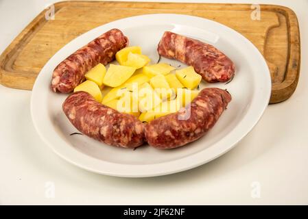 Link sausages with fresh baked potatoes on wooden cutting board   isolated on white with copy space. Stock Photo