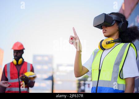 African-American female engineers wearing VR Headset look container cargo ship. Stock Photo