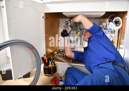 Plumber in uniform repairing a leak under the sink in a home with tools around. Horizontal composition. Stock Photo