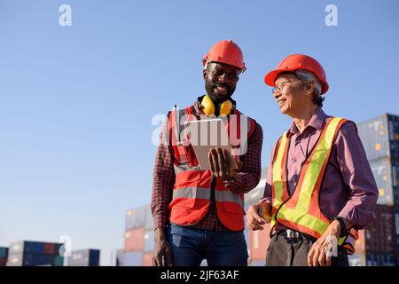 Happy African American and senior asian male worker using tablet during video call in a logistic shipping cargo containers yard. Stock Photo