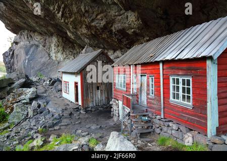 Norway landmark. Helleren old homes hidden beneath huge rock cliff in Jossingfjord. Stock Photo